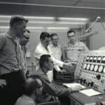 students and a teacher looking over a a large panel with dials and knobs in the late 1950s