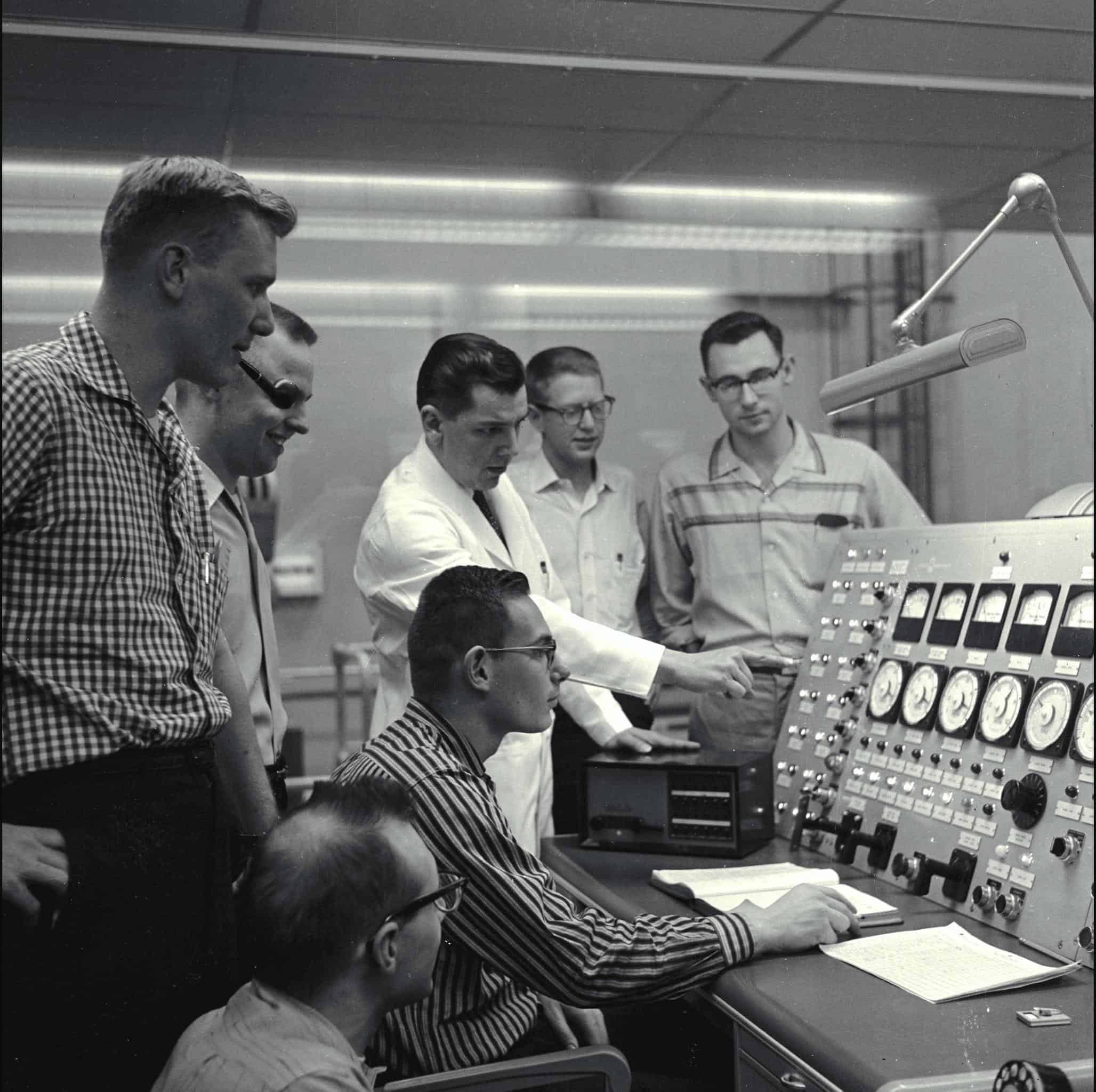 students and a teacher looking over a a large panel with dials and knobs in the late 1950s