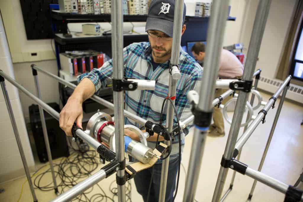 student in flannel wearing a detroit tigers ballcap in a laboratory with metal pipes and a canister