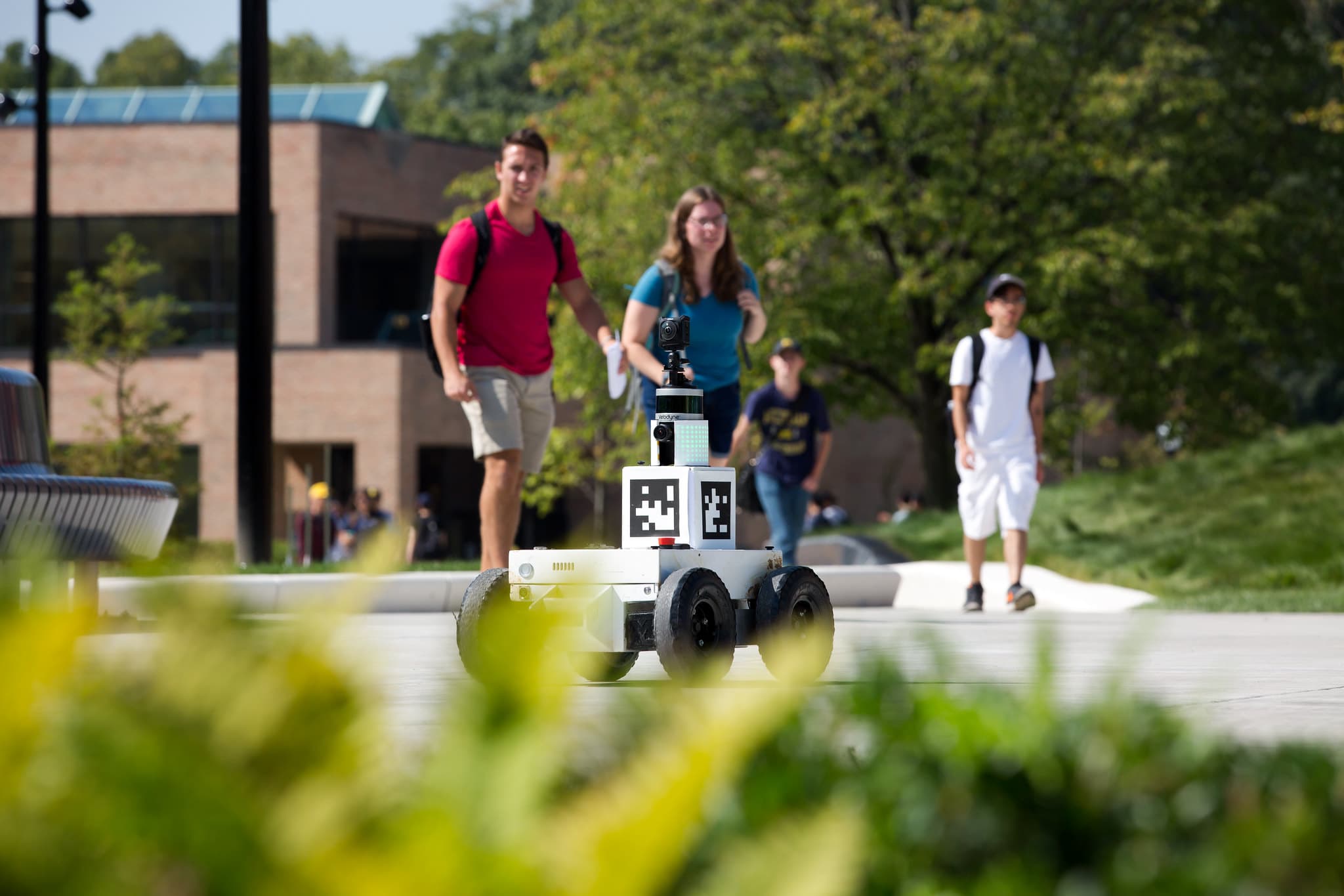 a robotic car moving across campus with onlookers behind