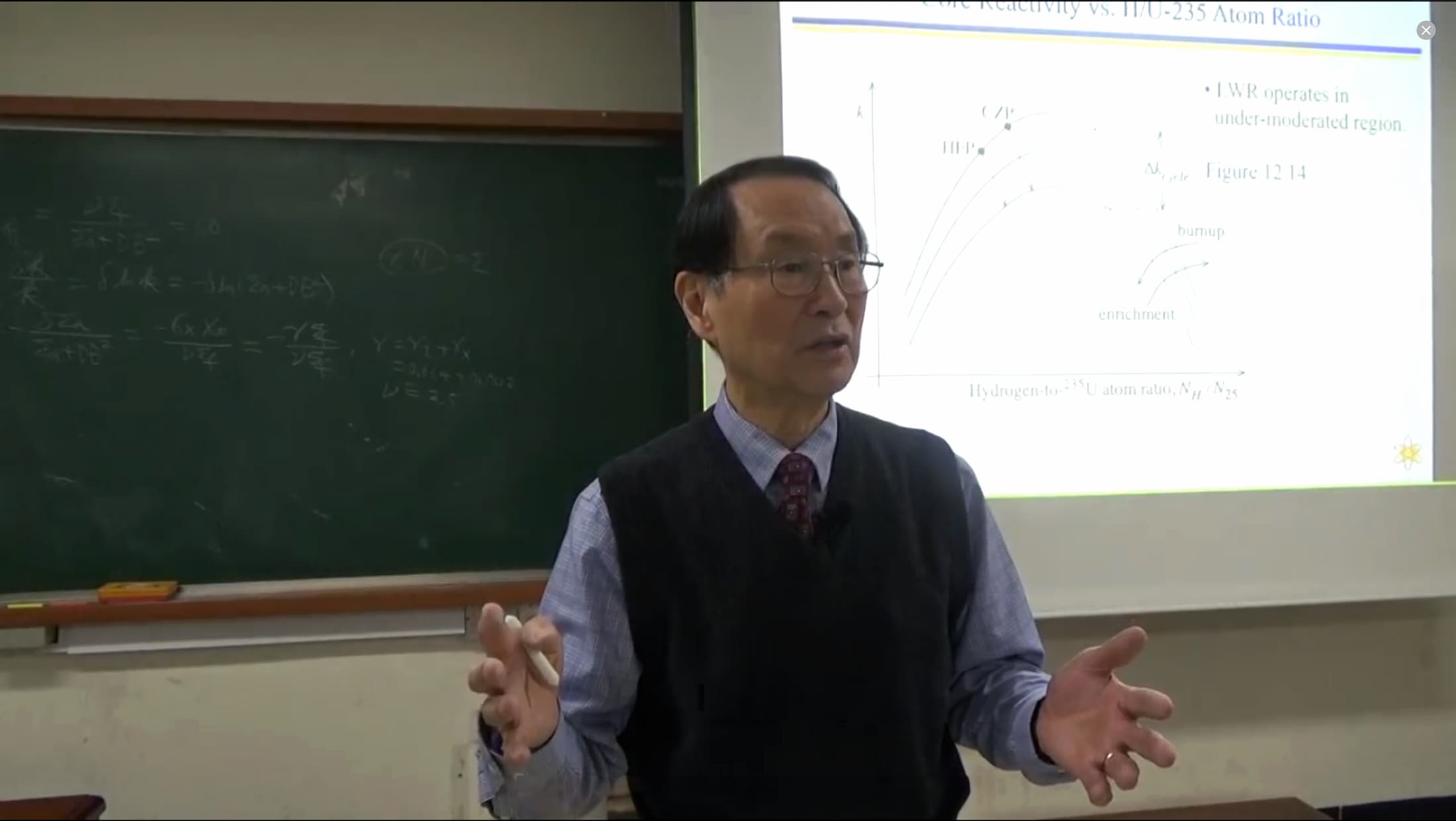 man speaking in front of a chalkboard and projector screen