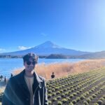 a man in front of crops, a lake, and a volcano