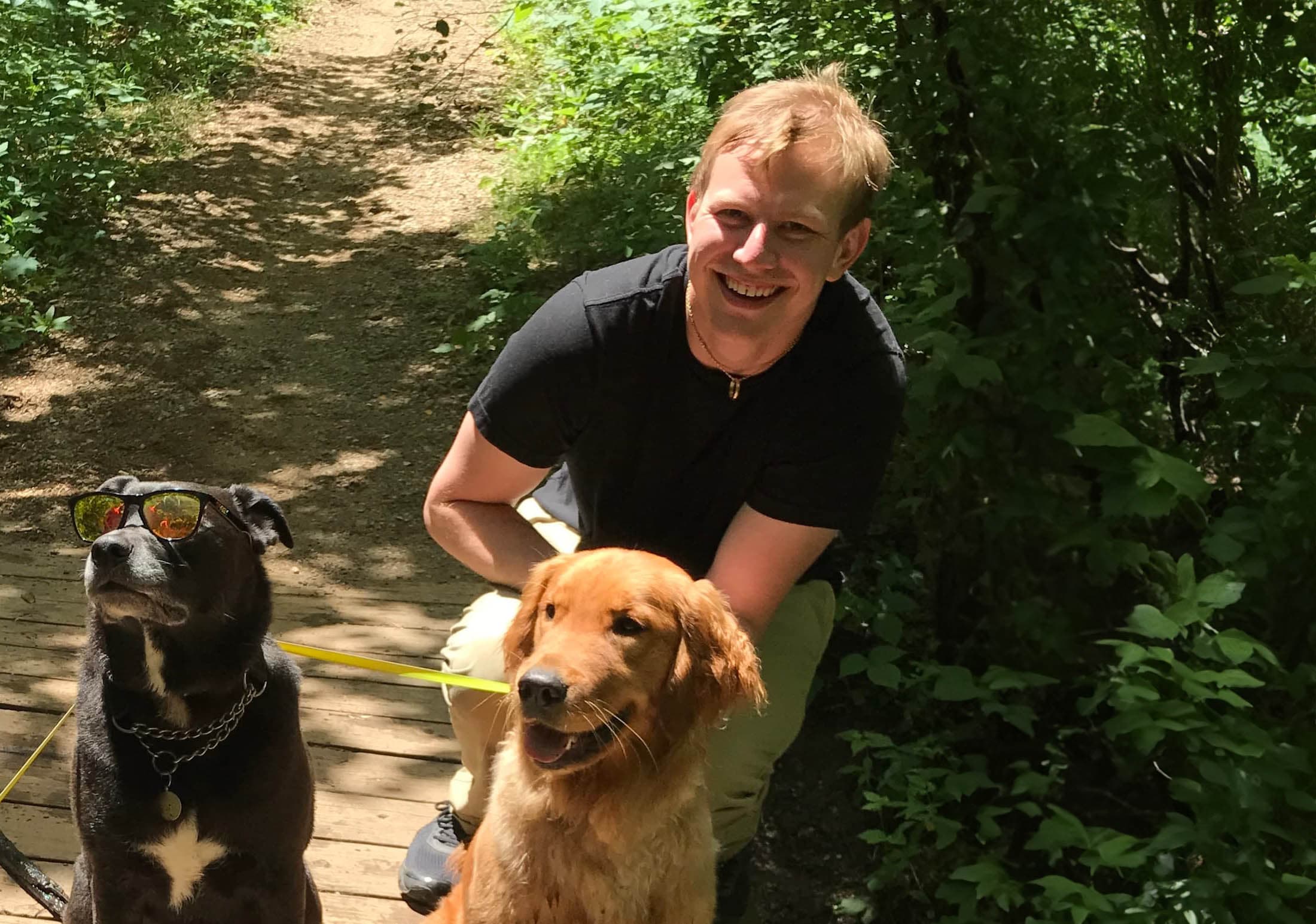 Juliusz Kruszelnicki with a black lab and a golden retriever on a wooden bridge on a hike