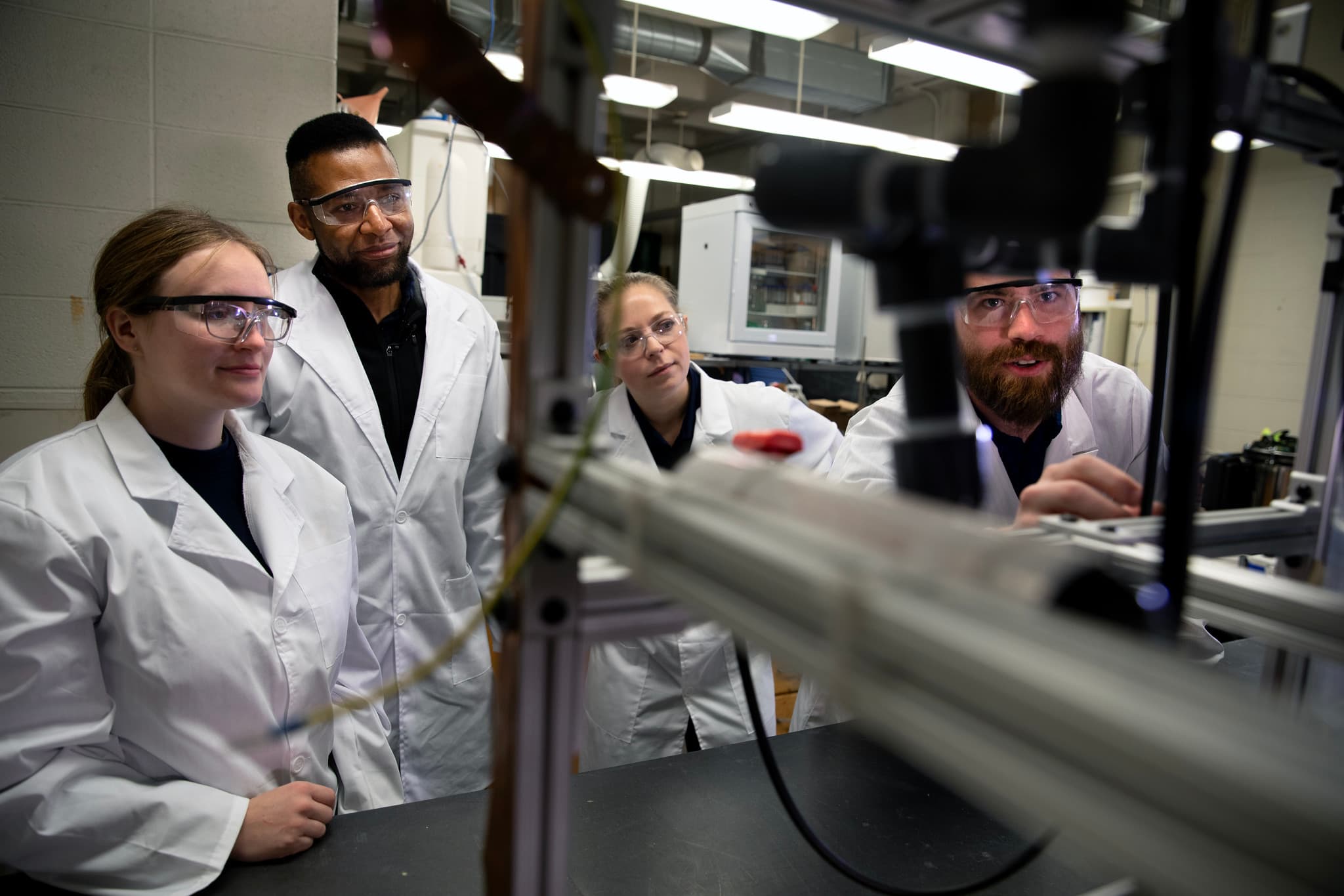 四名身穿实验室外衣的科学家在研究实验室检查设备。