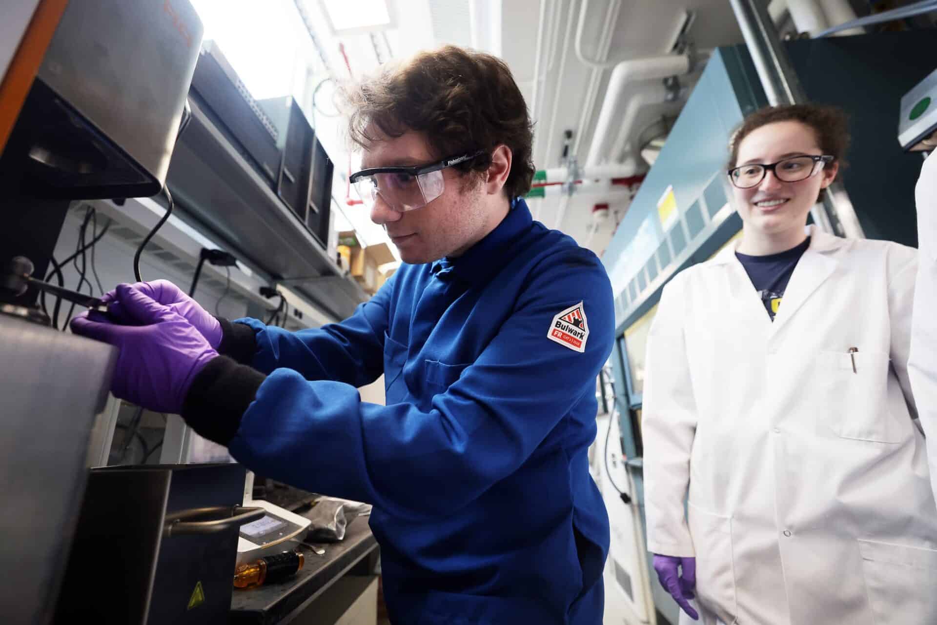 Two scientists in lab coats and protective eyewear work together in a laboratory