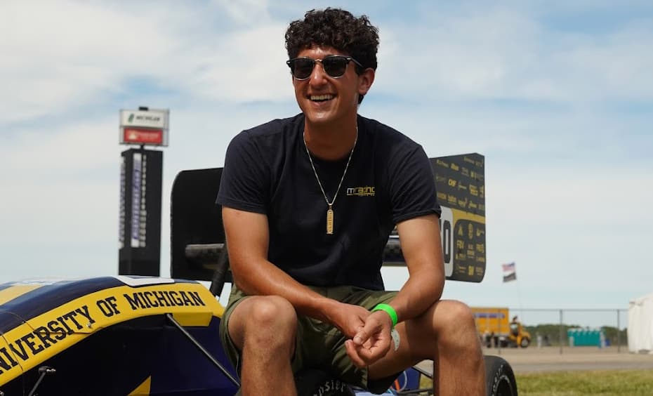 a man wearing a tshirt and sunglasses smiles while sitting on a racecar