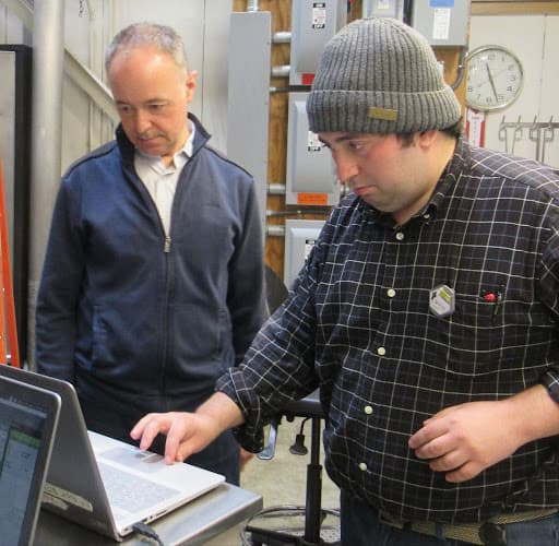 Two men look down at a computer screen in a laboratory setting while one man moves the mouse to zoom in.