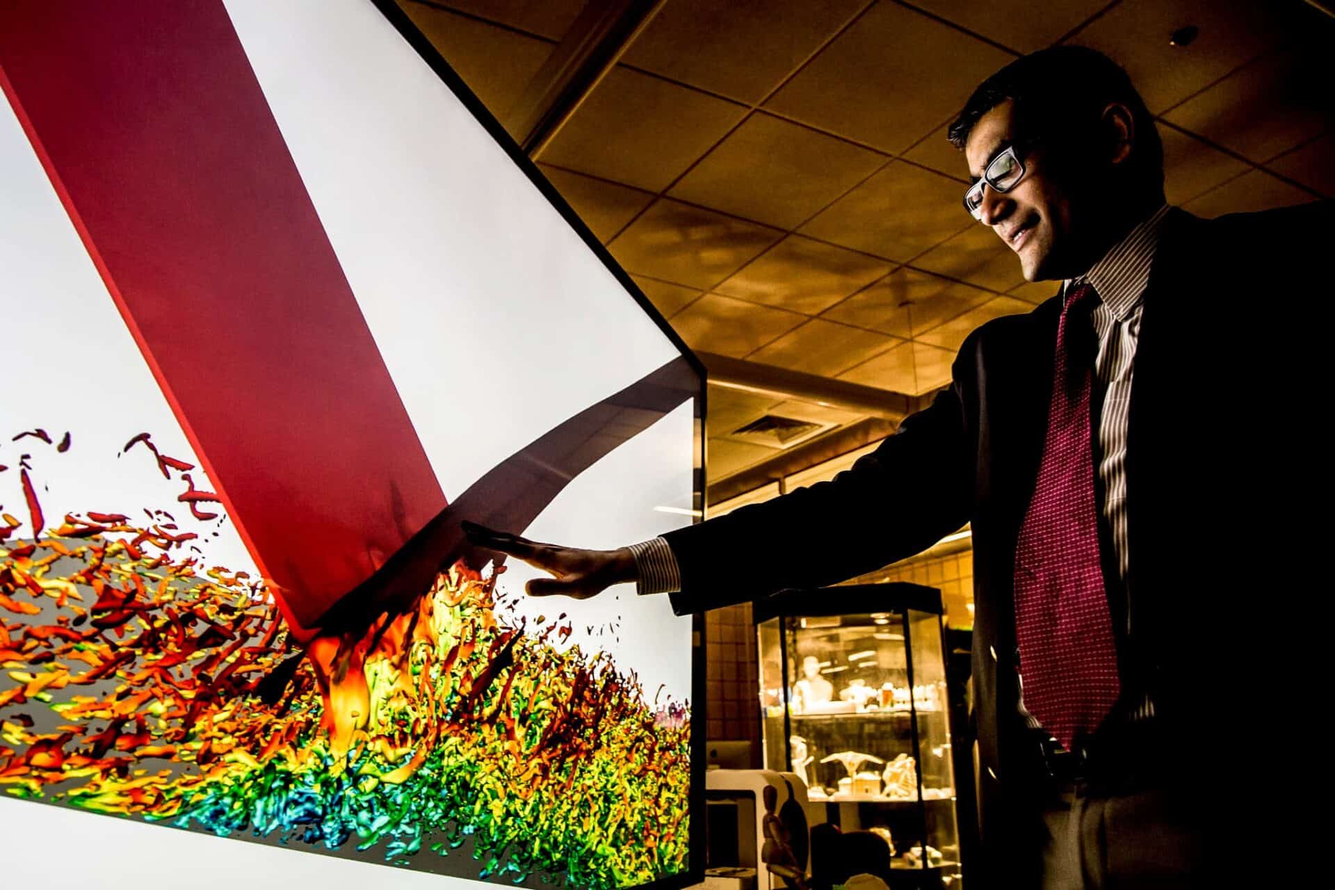 a man in a suit points at a brightly colored large computer screen